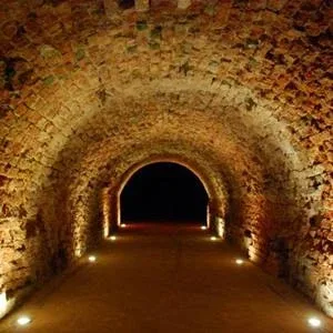 An old well-lit arched underground stone tunnel leading into the dark An old well-lit arched underground stone tunnel leading into the dark