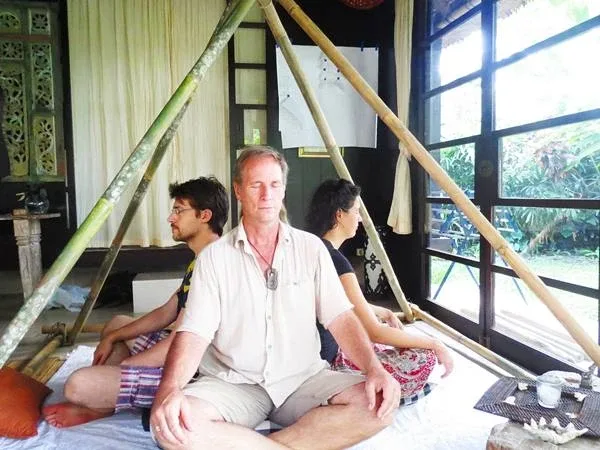 Four people sitting tailor style with their backs together and their eyes closed in a small pyramid created by wooden beams. Four people sitting tailor style with their backs together and their eyes closed in a small pyramid created by wooden beams.