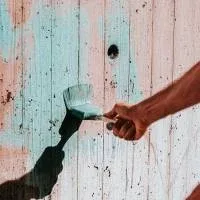A hand with a paintbrush, painting a formerly pink fence light blue A hand with a paintbrush, painting a formerly pink fence light blue