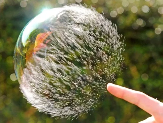 A big soap bubble just in the process of bursting because of a person's finger A big soap bubble just in the process of bursting because of a person's finger