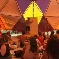 A man and a woman delivering a work talk inside a huge tent, a group of people are sitting on the ground and listening to them A man and a woman delivering a work talk inside a huge tent, a group of people are sitting on the ground and listening to them