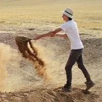 A man standing on a mountain of dirt empting a shovel of dirt A man standing on a mountain of dirt empting a shovel of dirt
