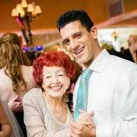 An older lady and a young man dancing together at an indoors celebration, grinning at the camera. An older lady and a young man dancing together at an indoors celebration, grinning at the camera.