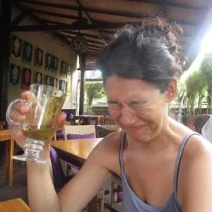 A woman with a screwed up face at a restaurant table with a half-full glass in her hand A woman with a screwed up face at a restaurant table with a half-full glass in her hand