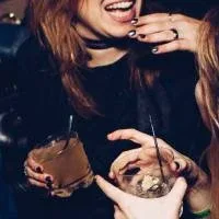 Two dressed up women talking and gesticulating with each other, a drink with a straw in their hands Two dressed up women talking and gesticulating with each other, a drink with a straw in their hands