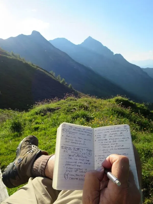 A person writing in their Beep! Book that's balanced on their legs, somewhere in nature with a very nice view of grassy hills and blue sky A person writing in their Beep! Book that's balanced on their legs, somewhere in nature with a very nice view of grassy hills and blue sky