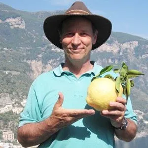 A man in a mint coloured shirt and a brown hat, proudly presenting a big citrus fruit he's holding in one hand A man in a mint coloured shirt and a brown hat, proudly presenting a big citrus fruit he's holding in one hand