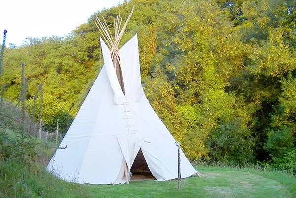 A big white tipi standing in front of a bright green forest A big white tipi standing in front of a bright green forest