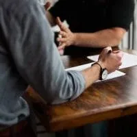 The arms and torso of two men having a discussion at a dark wooden table The arms and torso of two men having a discussion at a dark wooden table