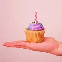 A hand holding a cupcake with violet icing and a blown-out candle A hand holding a cupcake with violet icing and a blown-out candle